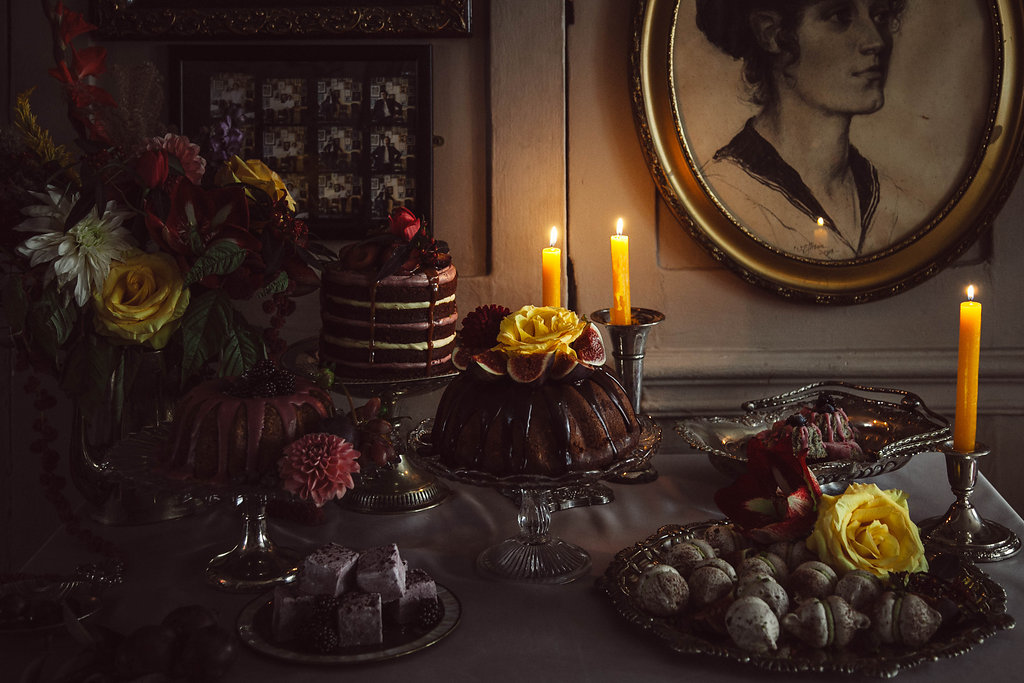 a dessert table of delicious cakes featuring layer cakes, bundt cakes, filled meringues and marshmallows with yellow candles and decadent flowers at The Union Club Soho