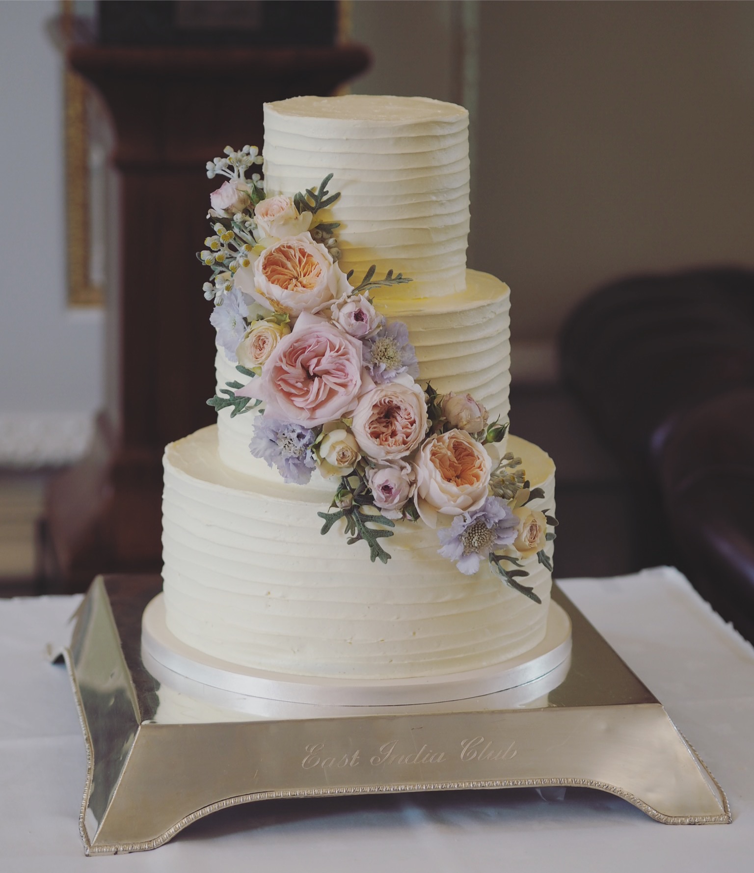 a 3 tier ribbed buttercream wedding cake with a cascade of fresh flowers, juliette david austin roses, scabious and foliage at The East India Club London