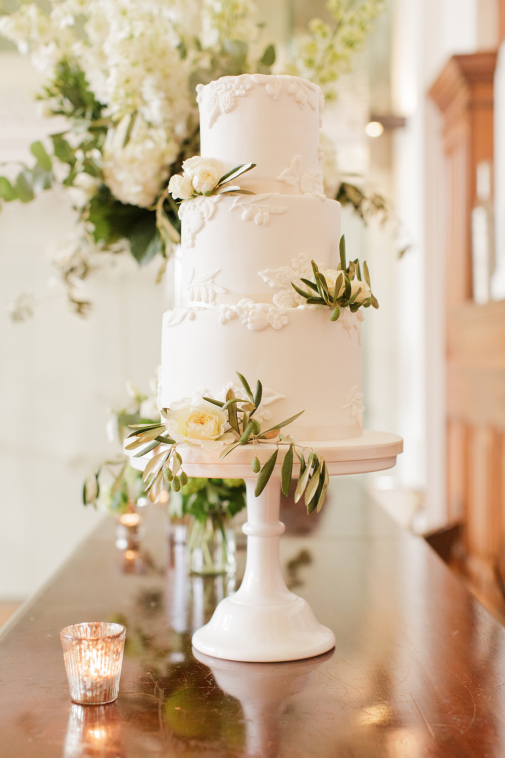 a 3 tier white wedding cake with bas relief detailing, fresh white roses and olive foliage at the Town Hall Hotel Bethnal Green