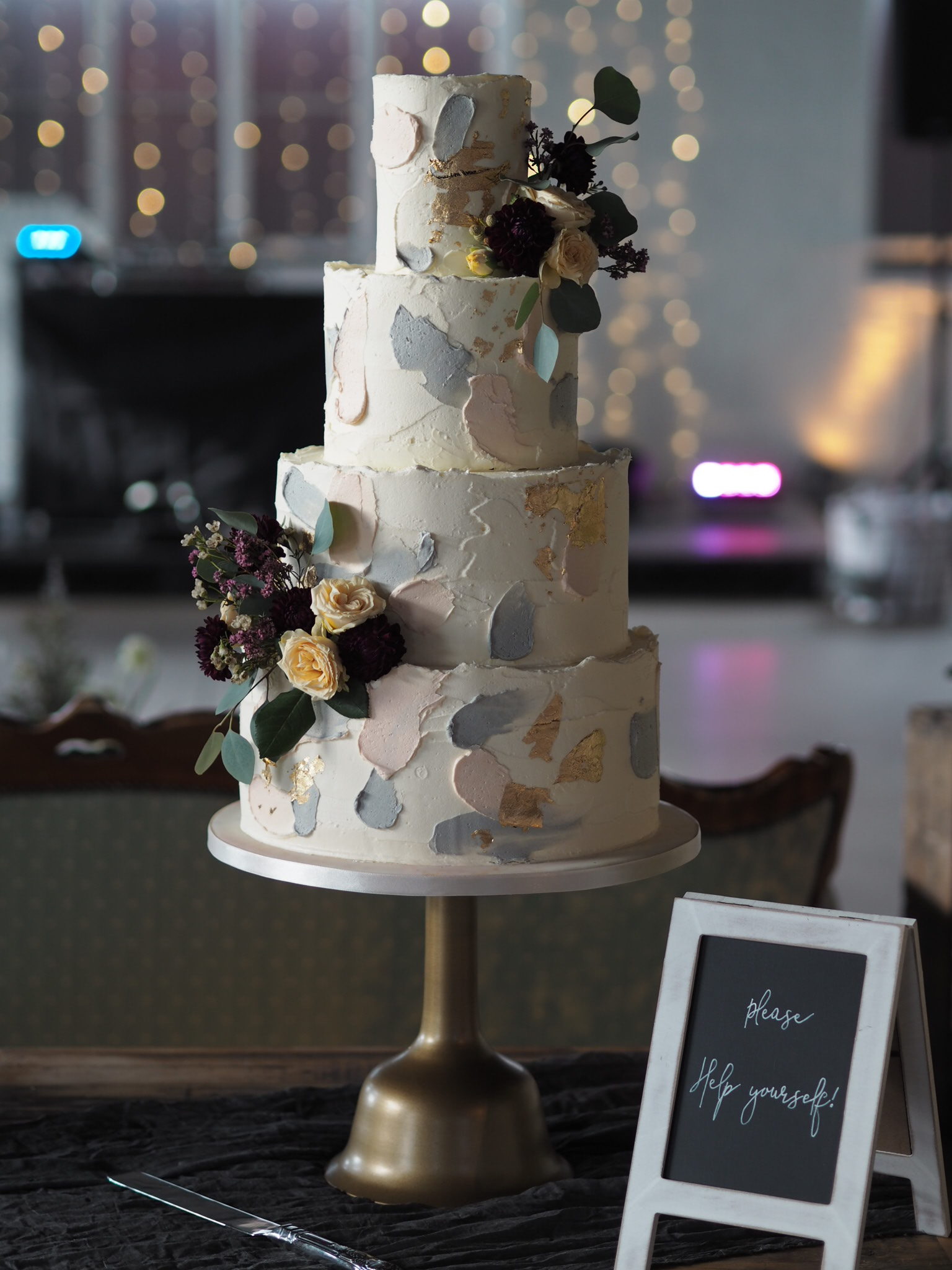 a 4 tier buttercream wedding cake with painted brushstrokes in blush and grey with edible gold leaf and 2 statement flowers arrangements at the chainstore trinity buoy wharf wedding venue east london