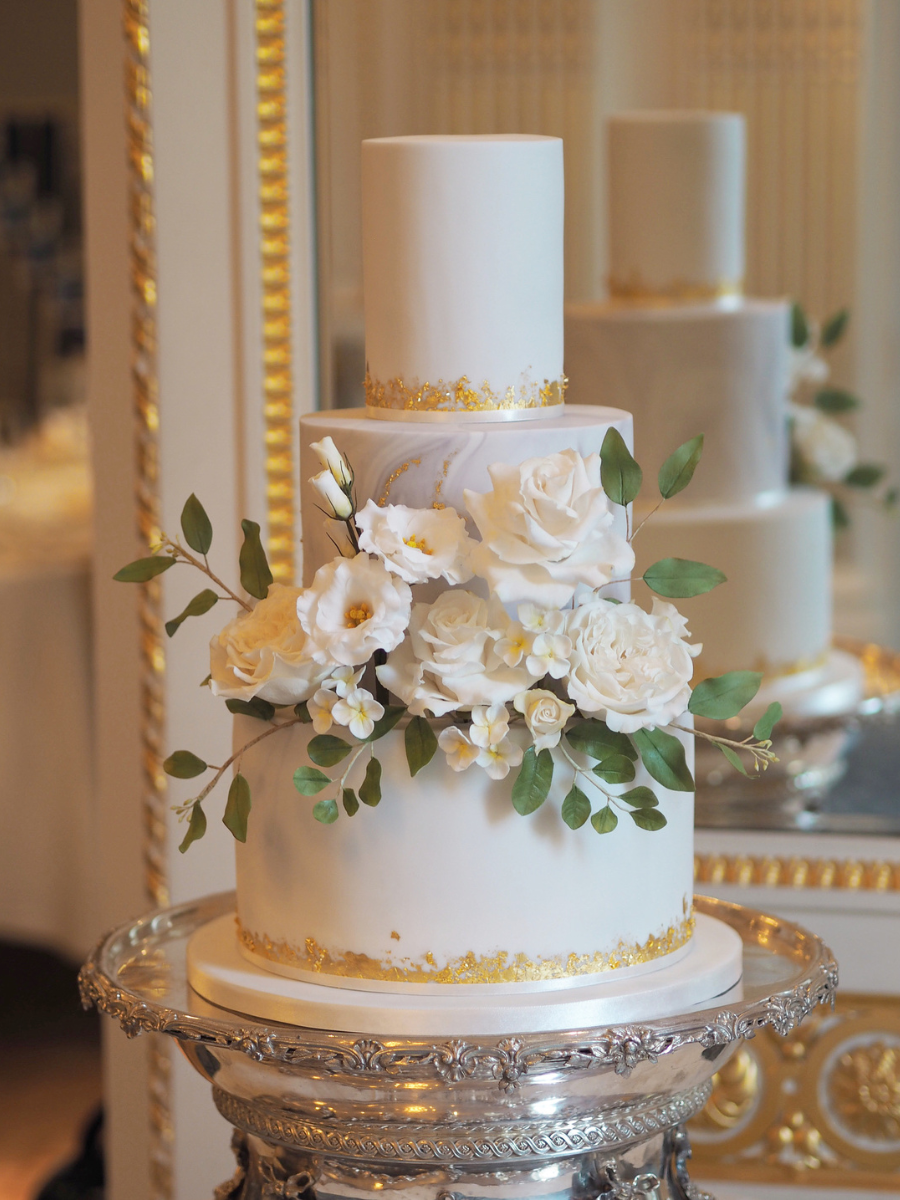 a 3 tier white, marble and gold leaf wedding cake with a large statement sugar flower arrangement with white roses, white lisianthus, white hydrangea and green foliage at The Mandarin Oriental Hotel Hyde Park